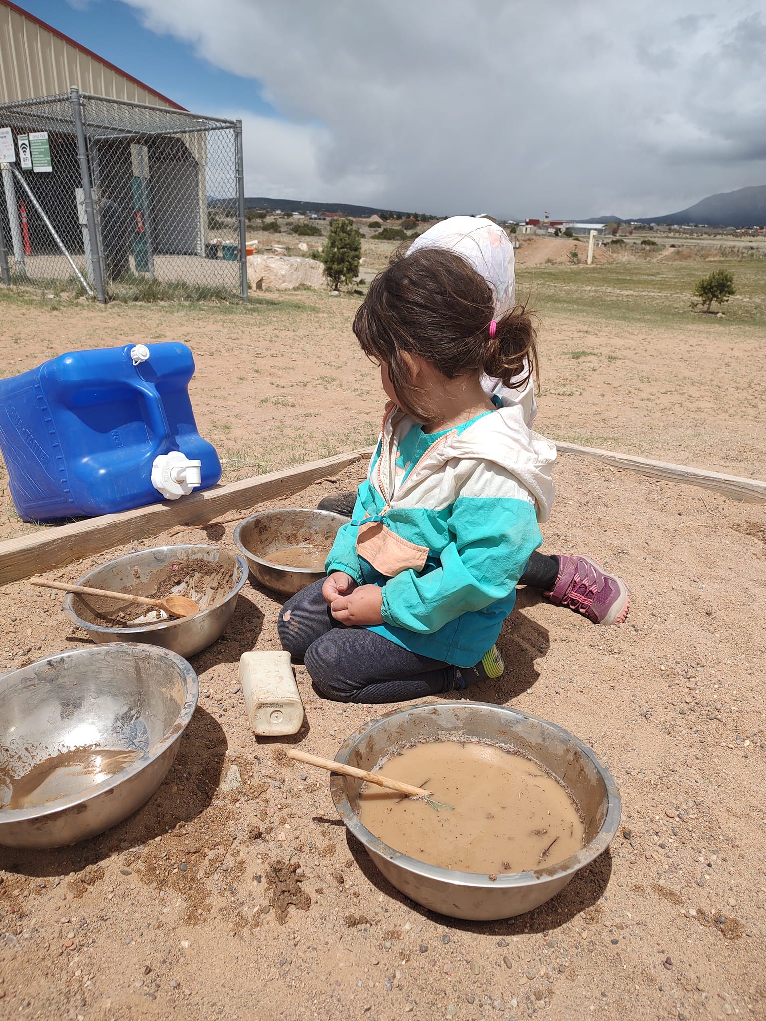 children mix sand and water in metal bowls